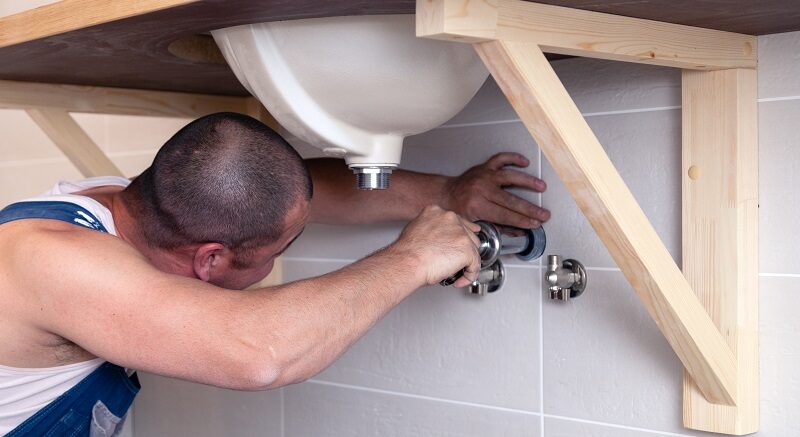 Closeup male plumber worker in blue denim uniform, overalls, fix